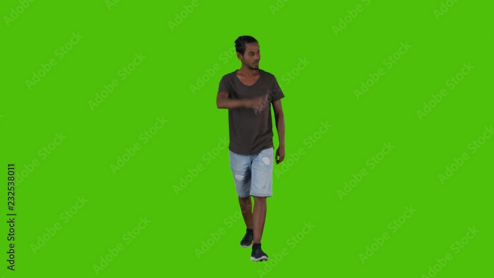 Casually dressed young man walking, waving hello and looking around happily in a full frontal shot over a green background. Casually dressed young man walking, waving hello and looking around happily in a full frontal shot over a green background.