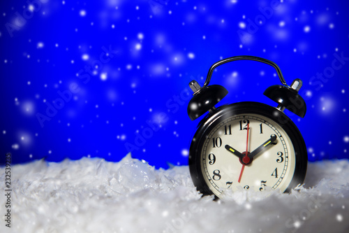 frozen vintage analog alarm clock with falling snow on blue background with copy space.