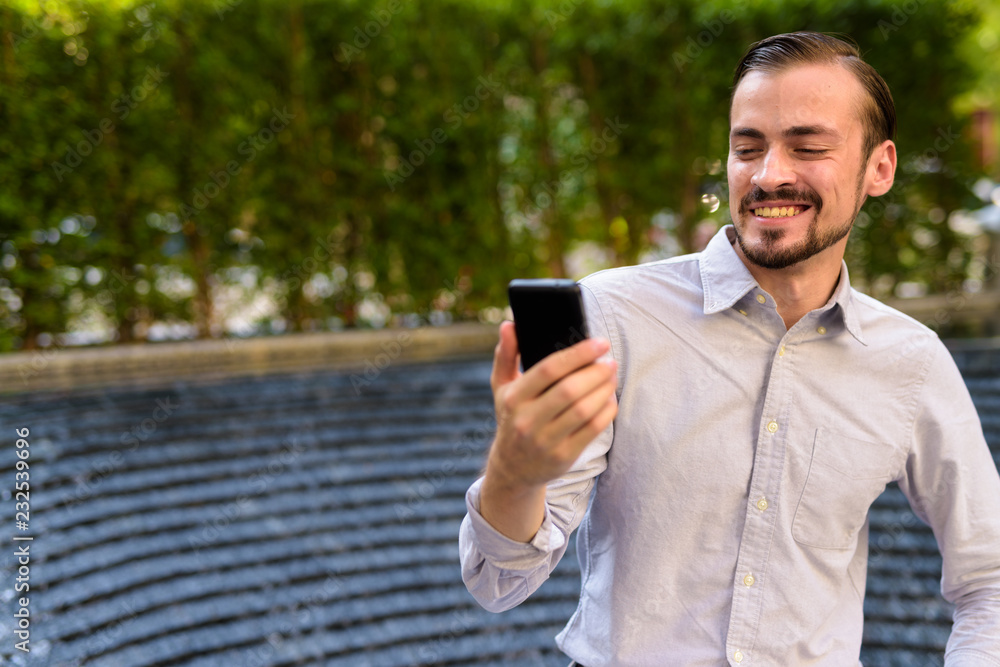 Happy young bearded fashionable man using mobile phone outdoors Happy young bearded fashionable man using mobile phone outdoors