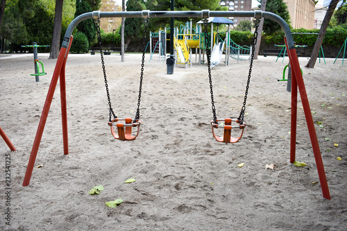 TWO ORANGE BASKETS OF A SWING ON THE LIGHT BROWN SAND OF A GROUND IN A PARK WITHOUT KIDS PLAYING IN A DAY OF AUTUMN