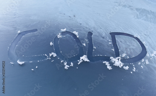 THE WORD COLD WRITTEN WITH A FINGER ON THE WINDSCREEN OF A VEHICLE SCRAPING THE ICE THAT THE COLD WINTER HAS GENERATED DUE TO BELOW ZERO TEMPERATURES IN THE MORNING