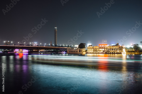 Cairo city center at night, long exposure with light trails of moving boats on the Nile river.