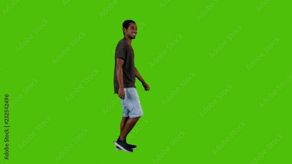 Casually dressed young man walking, waving hello and looking around happily in a full side shot over a green background. Casually dressed young man walking, waving hello and looking around happily in a full side shot over a green background.