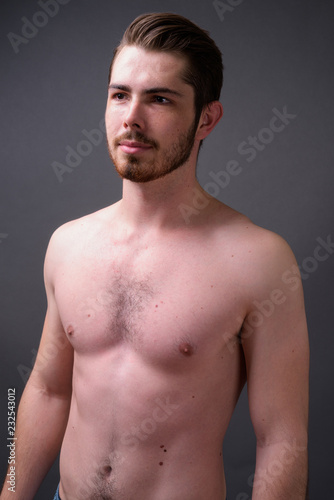 Young handsome bearded man shirtless against gray background