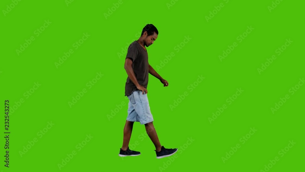 Casually dressed young man using an or or texting while walking, a full side shot over a green background. Casually dressed young man using an or or texting while walking, a full side shot over a green background.