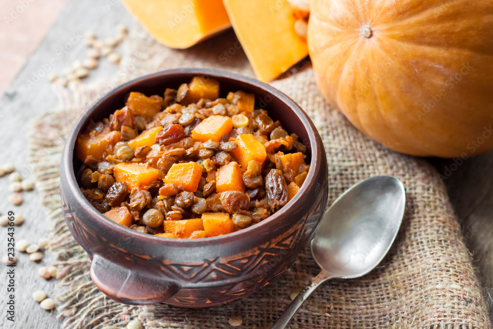 Fototapeta premium Homemade spicy curry with green lentils, pumpkin and raisins in rustic ceramic bowl