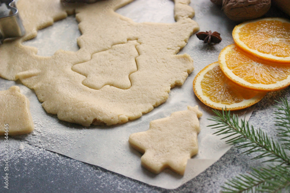 Preparation of Christmas cookies in the form of Christmas trees, fresh dough, spices scattered on the table, cinnamon, orange slices, nuts. Diet. Close-up background. Preparation of Christmas cookies in the form of Christmas trees, fresh dough, spices scattered on the table, cinnamon, orange slices, nuts. Diet. Close-up background.