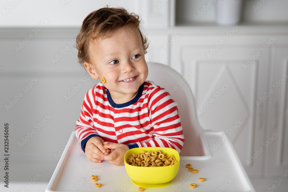 Smiling toddler sitting in high chair with bowl of cereal