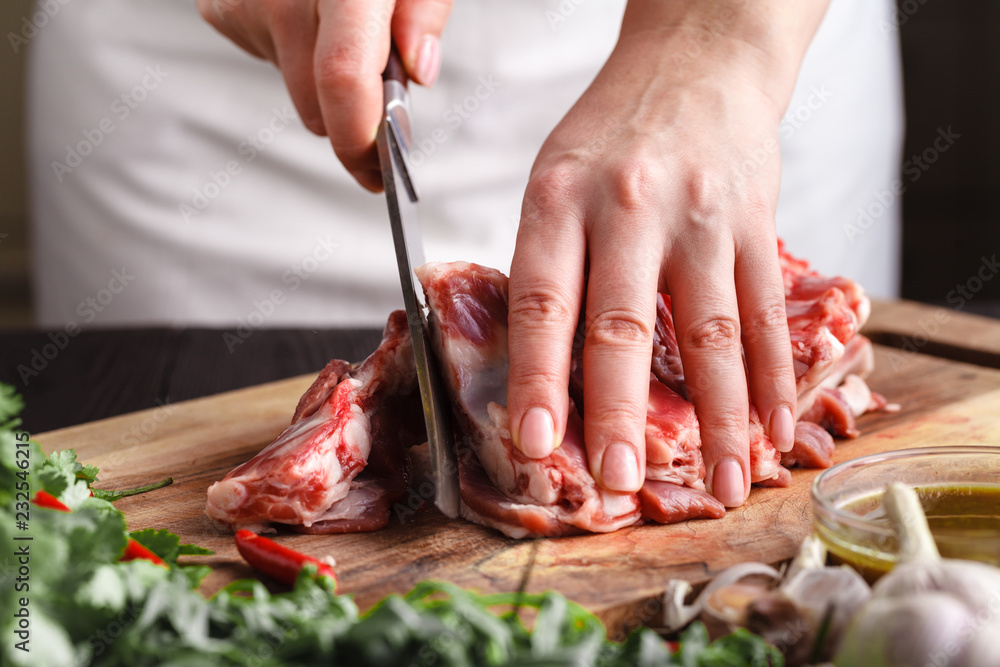 The concept of cooking meat. The chef, the butcher, cuts raw meat with beef, lamb, veal, holding a knife in his hand, on a wooden table, next to lie raw vegetable