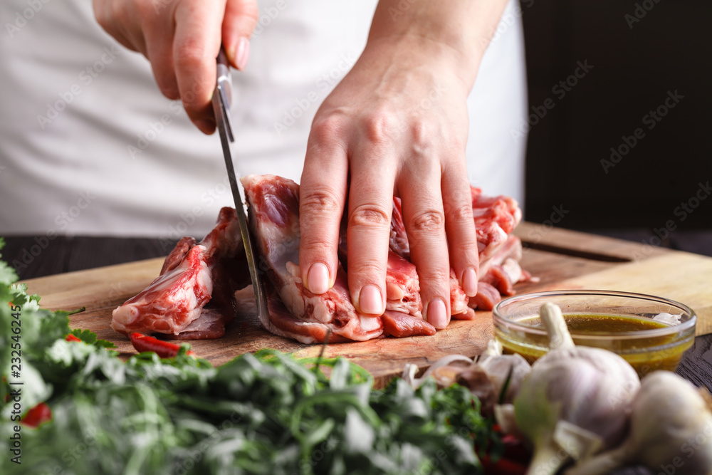 Female Chef cutting raw lamb meat on wooden board prepared for cooking