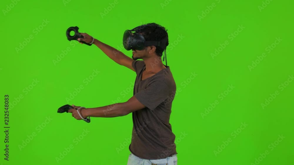 Playing a video game happily in a VR by a young man over a green screen, using remotes, casual look