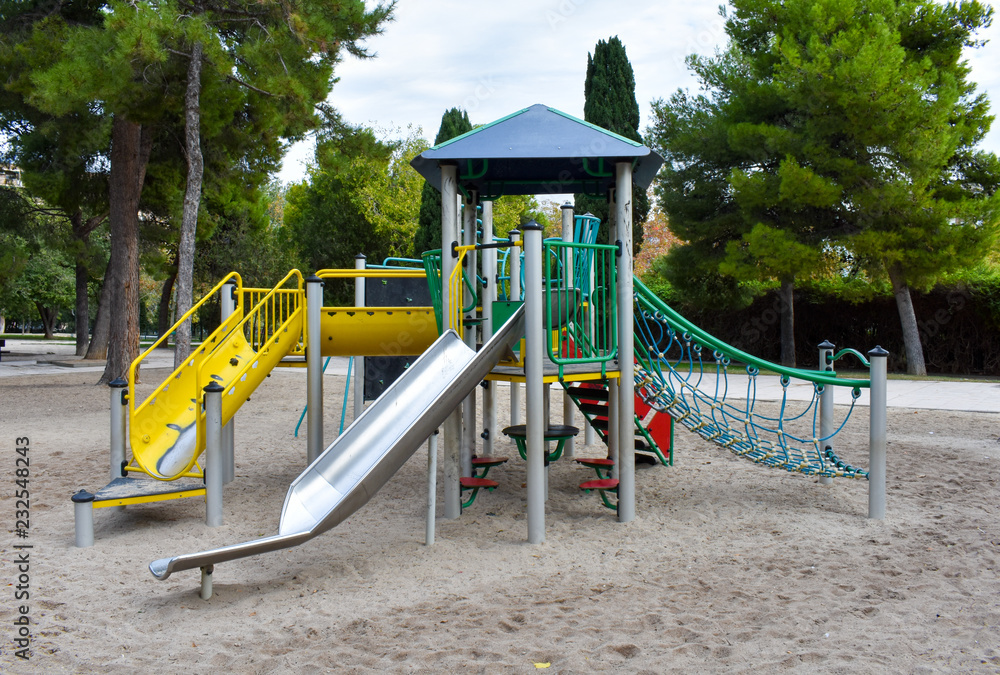PLAYGROUND ON YELLOW SAND FOR PLAYING KIDS IN AN EMPTY PARK PLENTY OF PINE TREES IN A DAY OF AUTUMN PLAYGROUND ON YELLOW SAND FOR PLAYING KIDS IN AN EMPTY PARK PLENTY OF PINE TREES IN A DAY OF AUTUMN