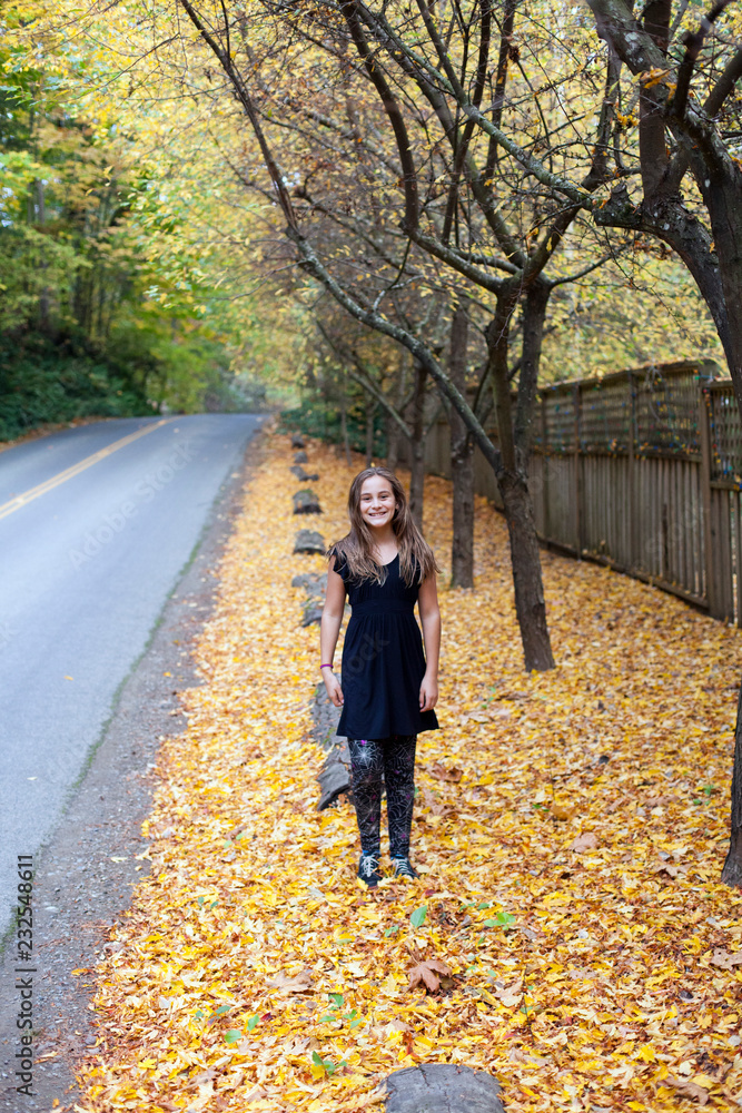 Girl in black walks in yellow leaves next to a road Girl in black walks in yellow leaves next to a road