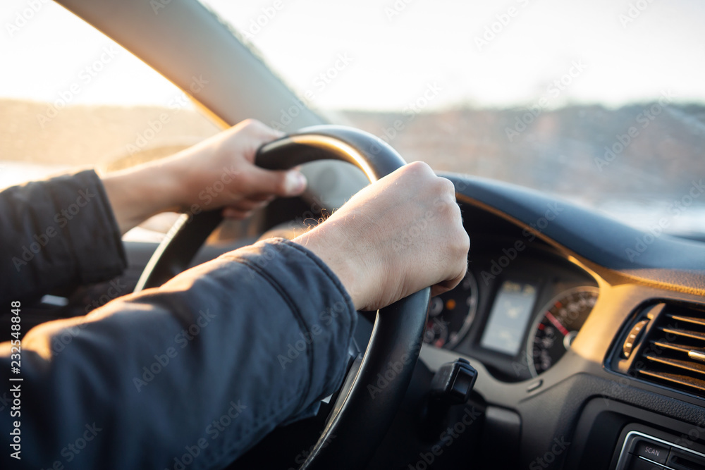 Driver's hand on steering wheel of car in cabin.