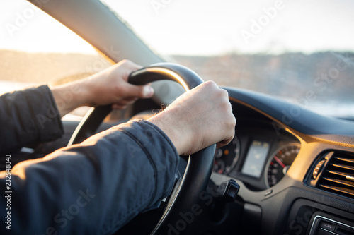 Driver's hand on steering wheel of car in cabin.