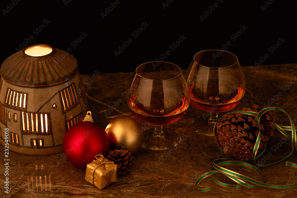pair of glasses of liquor on decorated Christmas table with candle lamp and black background