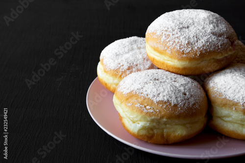 Homemade donuts with powdered sugar on pink plate over black background, side view. Copy space.