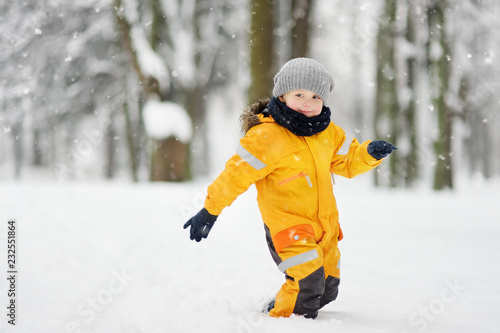 Cute little boy in yellow winter clothes walks during a snowfall