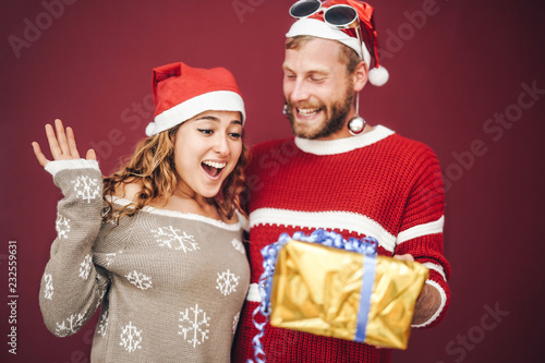 Happy boyfriend surprising his girlfriend giving her a christmas present - Young couple having fun celebrating xmas holidays - Love, millennial relationship concept