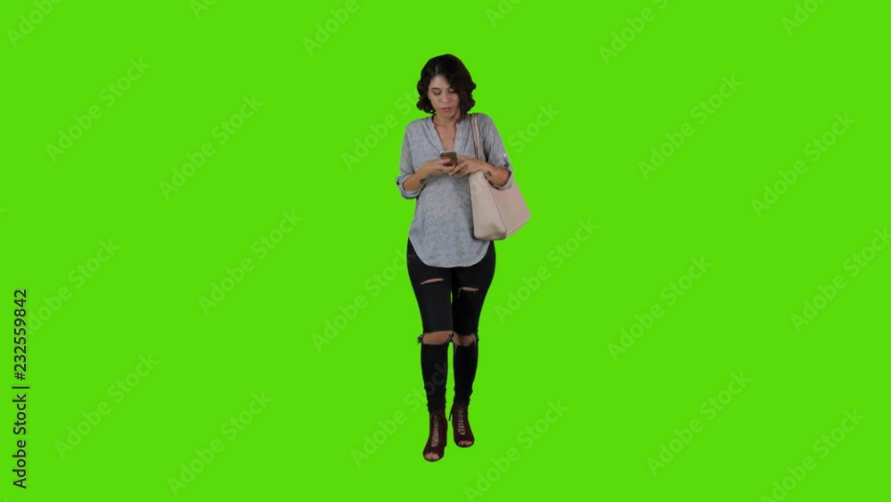 using an app happily while walking by a young woman over a green screen. casual look long frontal shot. using an app happily while walking by a young woman over a green screen. casual look long frontal shot.