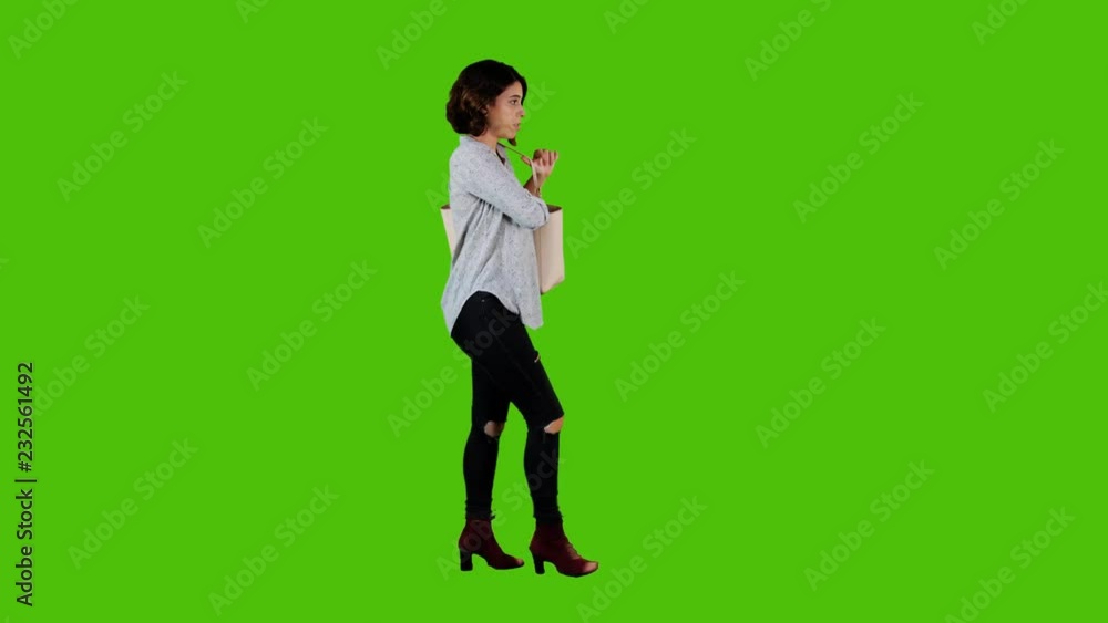 Answering a phone call happily while walking by a young woman over a green screen. casual look long side shot. Answering a phone call happily while walking by a young woman over a green screen. casual look long side shot.