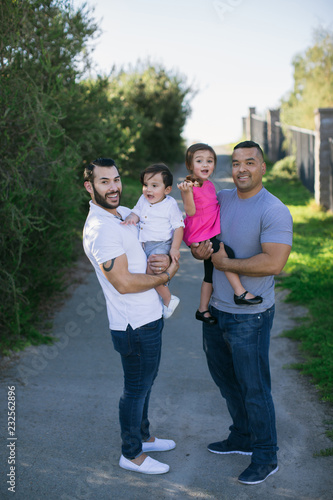 Family of four standing together outside - parents holding littl photo