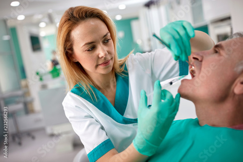 Female dentist giving anesthesia to senior male patient