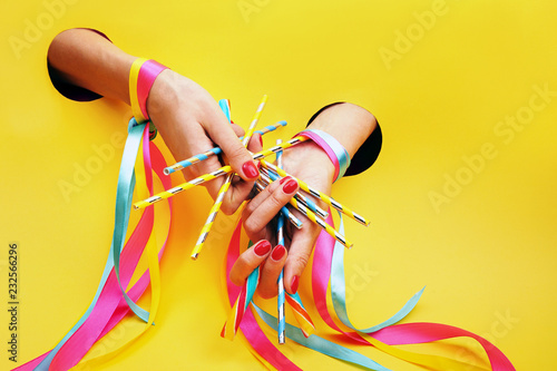 Cukierkowy manicure w stylu pin up. Dłonie z pomalowanymi paznokciami, udekorowane kolorowymi wstążkami na żółtym tle. photo