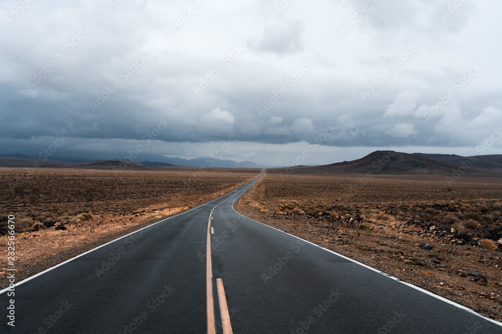 Fototapeta premium A road finds its way through Death Valley as a storm approaches and sunlight peaks through the clouds