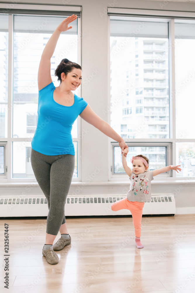 Young woman with child doing workout dancing in gym class to loose baby weight. Child-friendly fitness for mothers with kids toddlers. Lifestyle concept of parent activity. Young woman with child doing workout dancing in gym class to loose baby weight. Child-friendly fitness for mothers with kids toddlers. Lifestyle concept of parent activity.