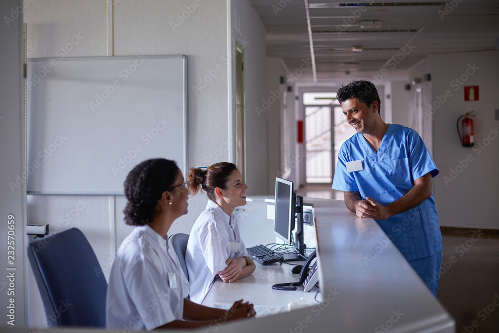 Hospital staff talking in a relaxed moment at the desk of a patient room floor Hospital staff talking in a relaxed moment at the desk of a patient room floor