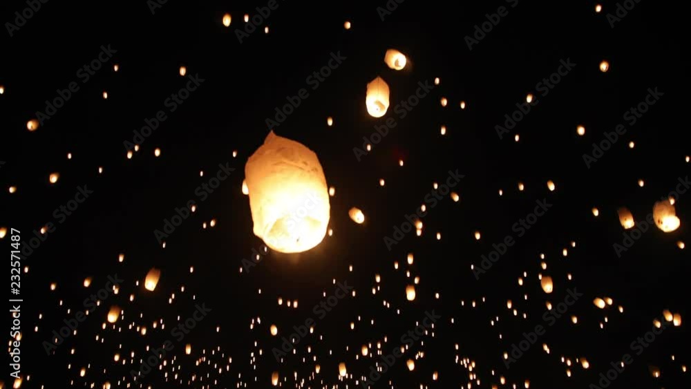 A person grabbing and letting go of a lantern sending it off into the night sky. A lantern lit by fire flys slowly off into the air. Close up up a persons hands holding a lantern.
