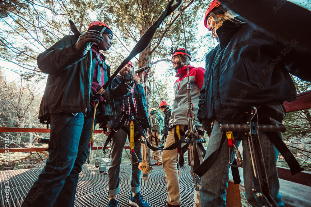 A group of friends laugh and talk before going on an outdoor zip line course A group of friends laugh and talk before going on an outdoor zip line course