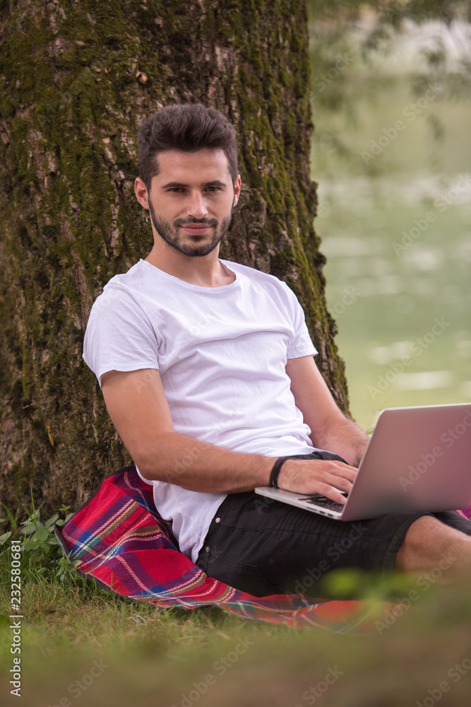 Obraz premium man using a laptop computer on the bank of the river