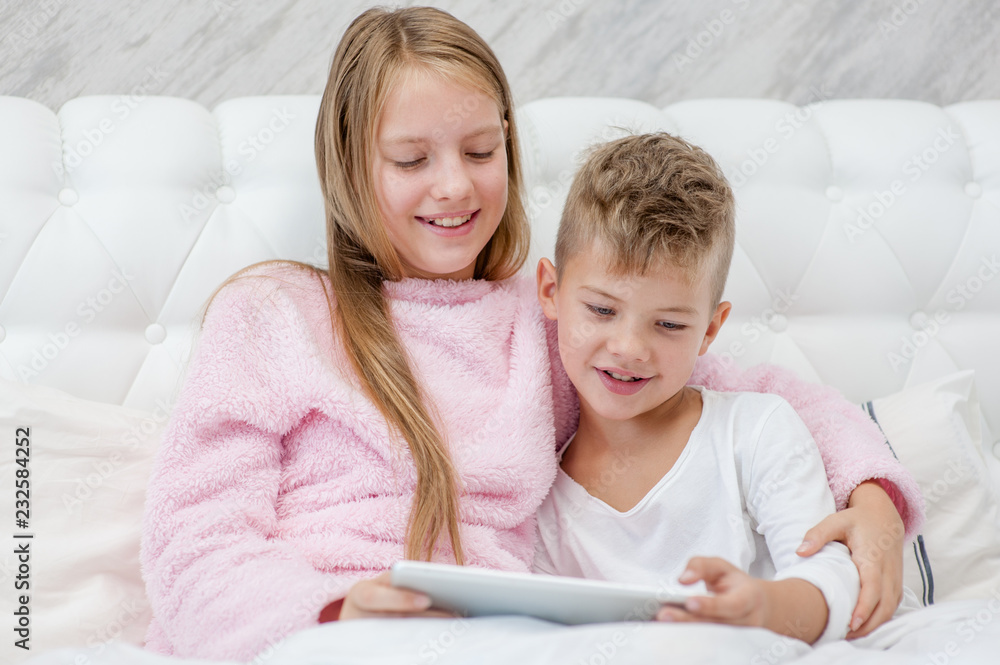 Happy girl and little boy using tablet pc on the bed Happy girl and little boy using tablet pc on the bed