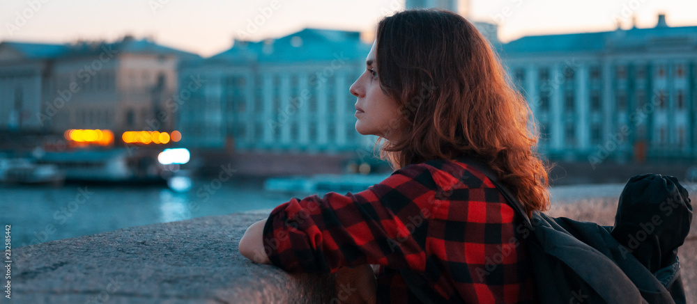 Obraz premium young beautiful girl tourist looks at the city on the background of the night city and the river, St. Petersburg, travel to Russia