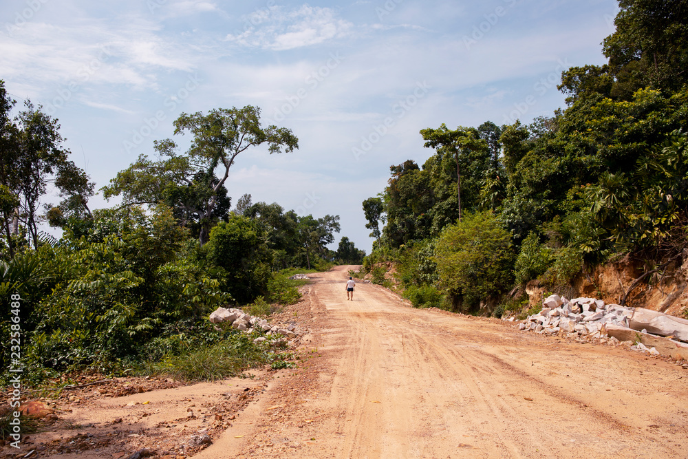 Empty road in forest and lonely tourist. Road construction site in green nature. Tropical island development.