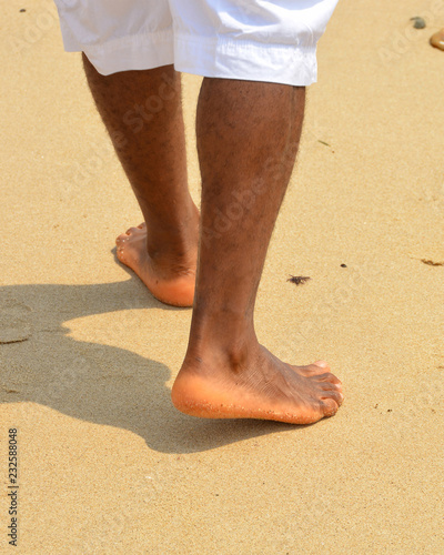 African american man walks on a sand beach. Close up of male feet and golden sand. Beach walk. Summer activity. Beautiful holiday background