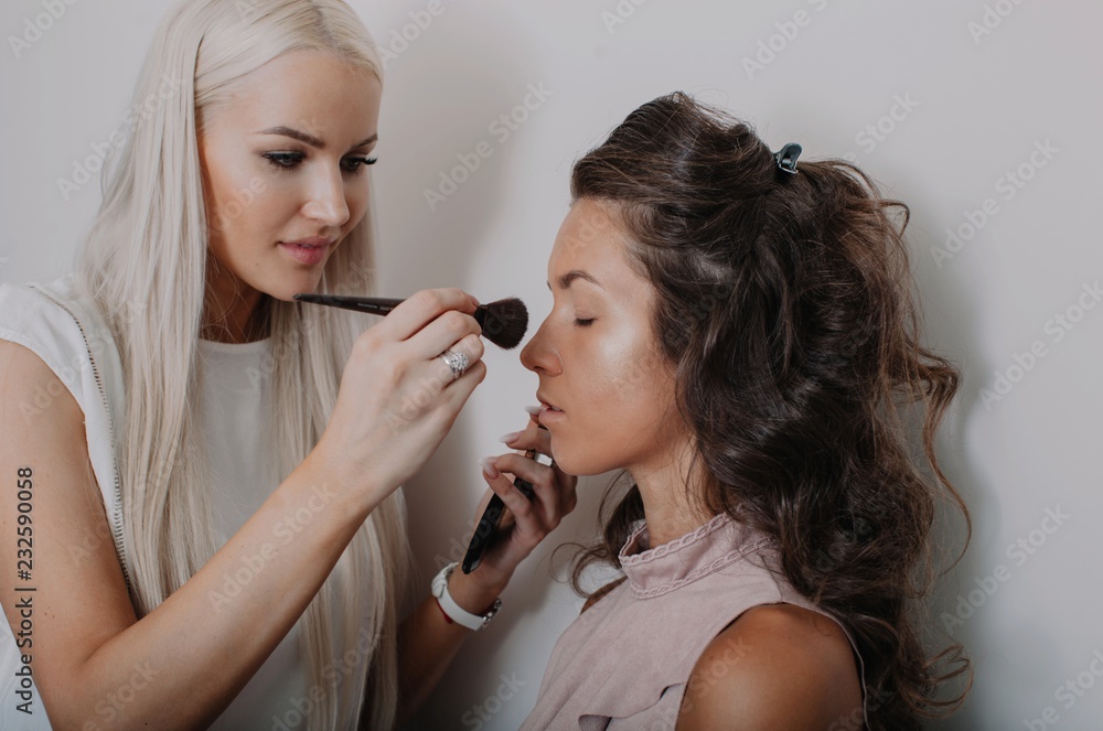Pretty makeup artist applying makeup to a model against white wall Pretty makeup artist applying makeup to a model against white wall