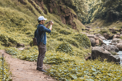Young Asian traveler man taking photo outdoors scenic nature background. Lifestyle and relaxation concept.
