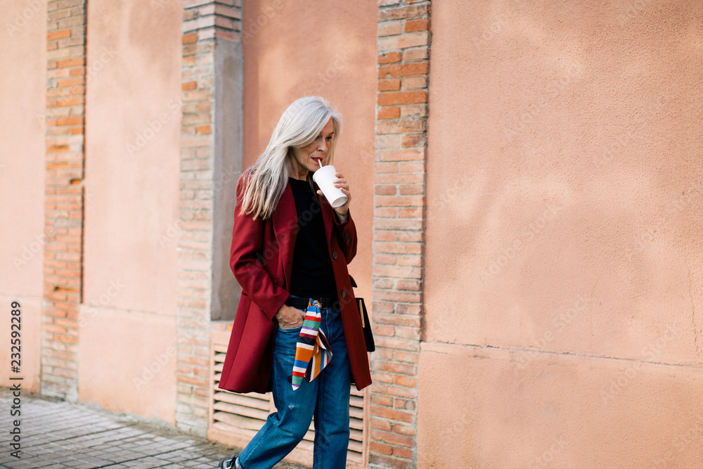 © Stocksy - Mature woman with grey long hair drinking a refreshment on the street. © Stocksy - Mature woman with grey long hair drinking a refreshment on the street.