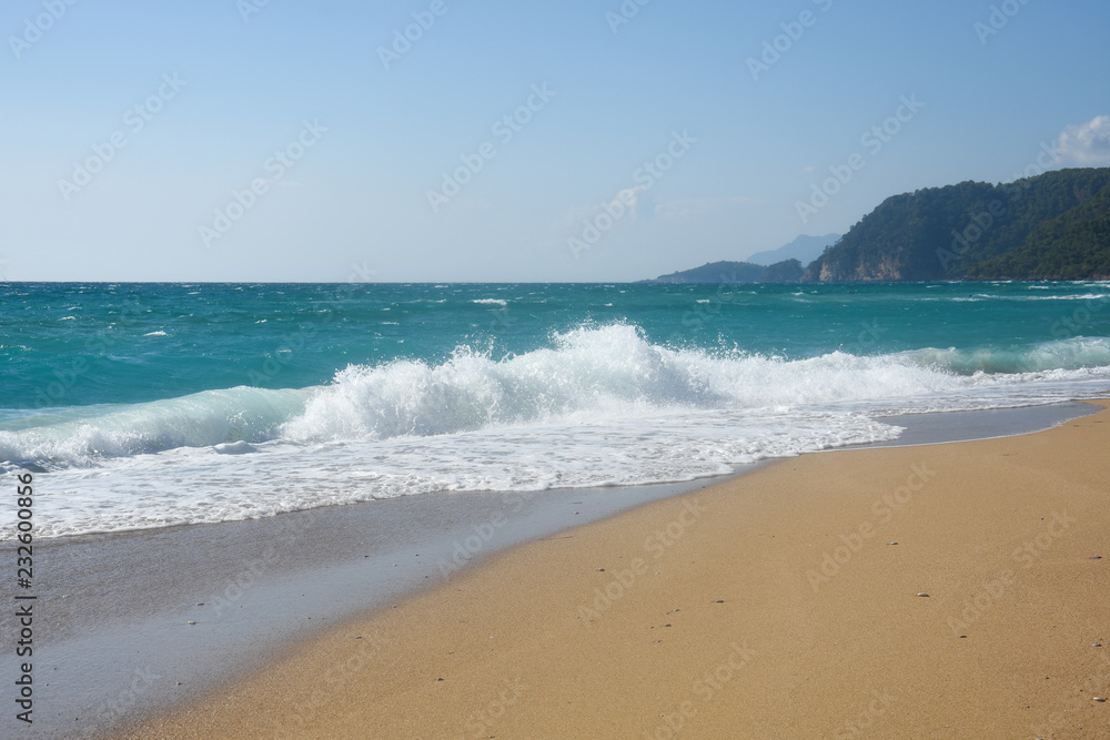 Big breaking wave on a sandy beach. Beautiful sandy beach with big sea waves on sunny summer day