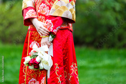 A Chinese bride in a traditional red dress holds a bouquet of flowers