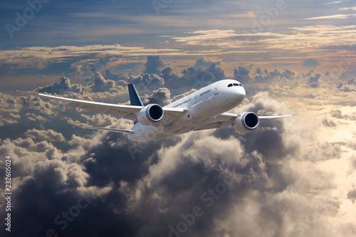 White passenger plane in flight. The plane flies against a background of clouds and mountain landscape. Aircraft side view.