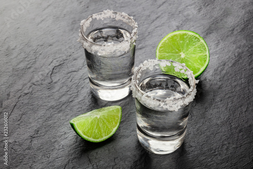 A photo of a tequila shots with lime slices on a black background with copy space