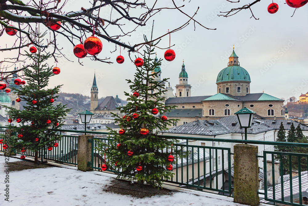 Fototapeta premium Piękny widok na zabytkowe miasto Salzburg ze słynną katedrą w Salzburgu w zimie, Austria. Choinki z czerwonymi bombkami na tle zimy Salzburg.