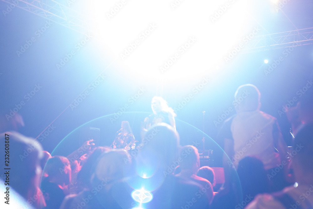 a crowd of people illuminated by floodlights, stand with their hands up and listen to a musical rock concert, blurred background a crowd of people illuminated by floodlights, stand with their hands up and listen to a musical rock concert, blurred background