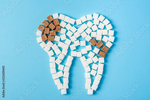 Sugar destroys the tooth enamel and leads to tooth decay. Tooth made of white sugar cubes and caries made of brown sugar cubes. Top view. Close up
