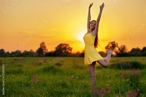 Happy cheerful girl is jumping on nature over the summer sunset background