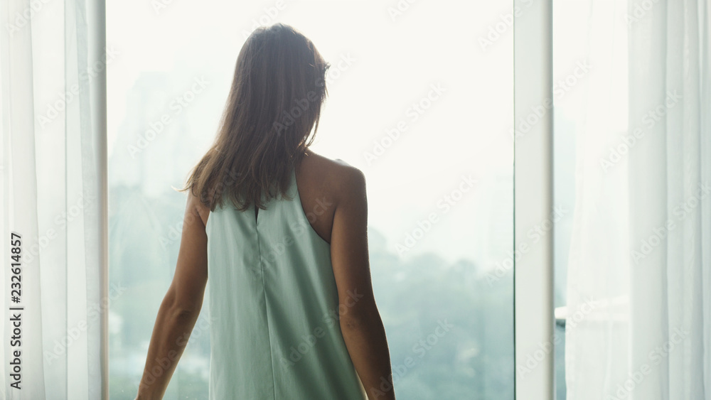 Young brown-haired woman looking through window to the city view. Young brown-haired woman looking through window to the city view.
